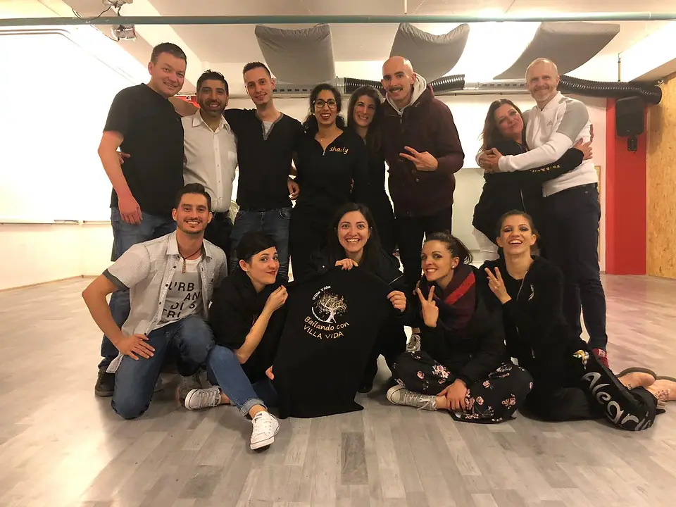Un groupe d’amis dans une salle de danse, accroupis autour d’un t-shirt « Bailando con Villa Vida ».