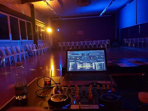 Une table de mixage et un ordinateur portable face à une salle vide, éclairée en bleu et orange.