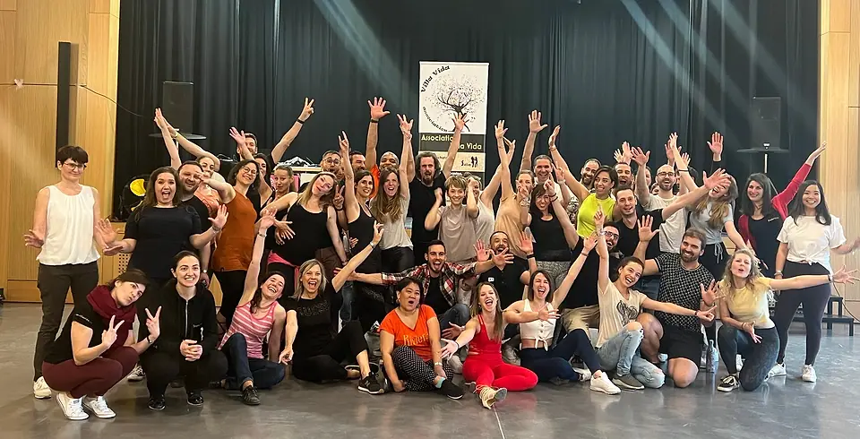 Photo de groupe : une cinquantaine de danseuses et danseurs, bras levés, devant le roll-up Villa Vida, sur une scène aux rideaux noirs.