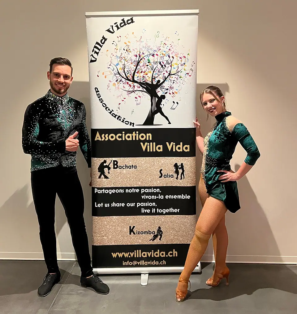 Un danseur et une danseuse en costumes de scène verts, de part et d'autre du roll-up Villa Vida ; au bas du roll-up, l'adresse info@villavida.ch.