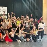 Photo de groupe : une cinquantaine de danseuses et danseurs, bras levés, devant le roll-up.