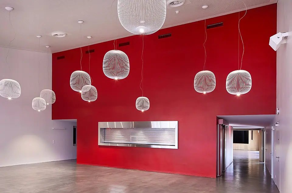 Le foyer de la salle des Utins : un grand mur rouge, des suspensions blanches en fil, un comptoir en inox.